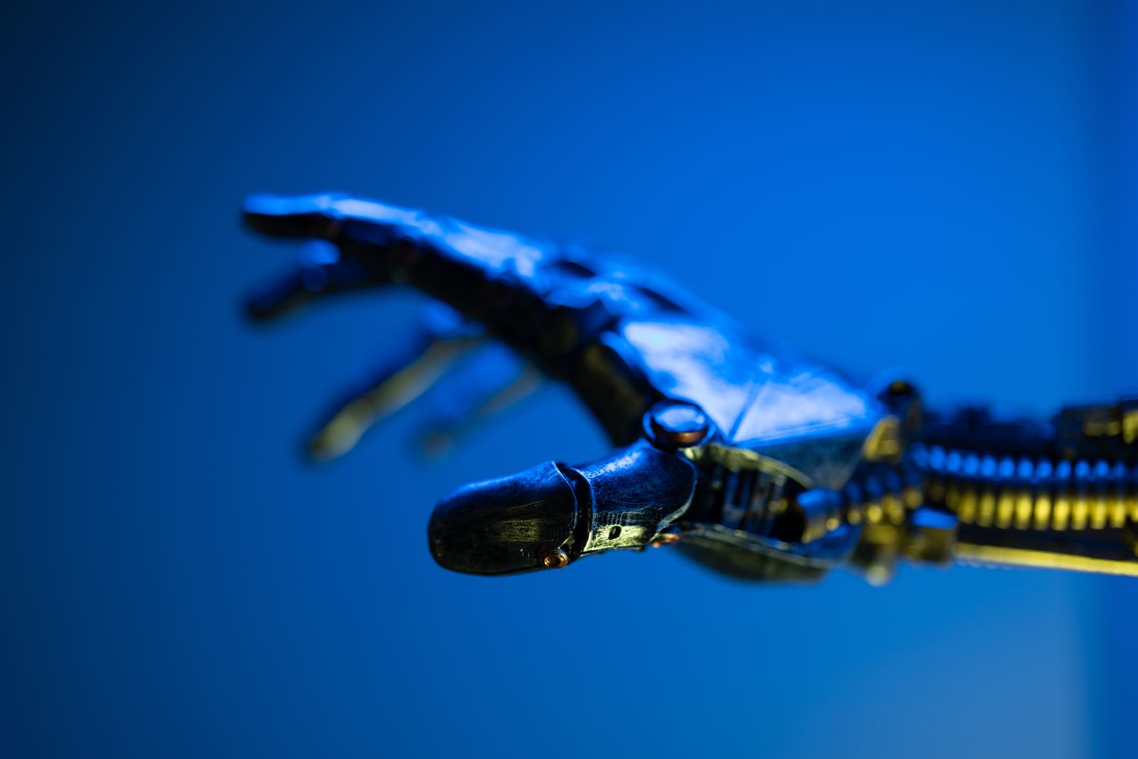 A jointed robotic hand reaching forward against a deep blue field.